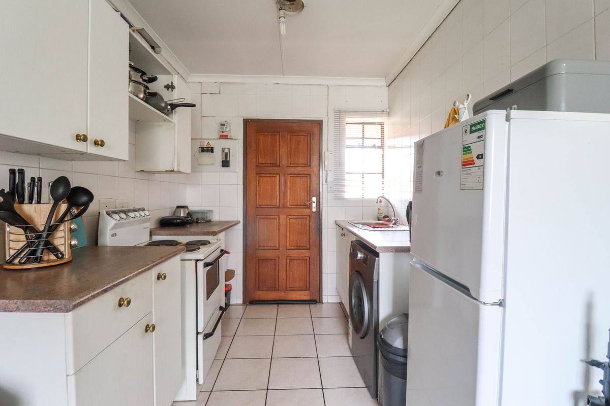 A functional galley-style kitchen featuring white cabinetry, tiled surfaces, and dedicated space for laundry appliances, leading to an exterior door.