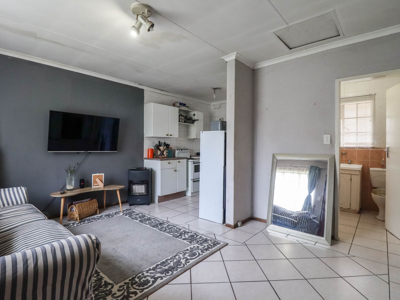 Open plan living area featuring tiled floors and an adjoining kitchen space, with visible ceiling damage requiring maintenance.