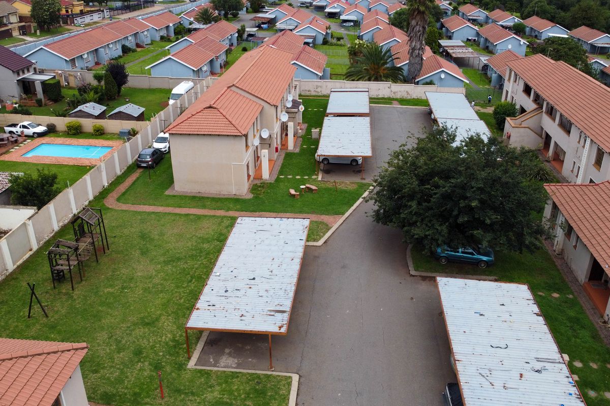 Aerial view of a residential apartment complex featuring multiple buildings with tiled roofs, communal garden areas, and covered carport parking bays.