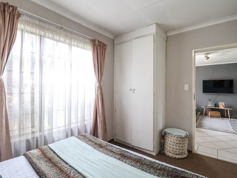 A bedroom featuring a built-in wardrobe, large window with natural light, and direct access to an adjacent living area with tiled flooring.