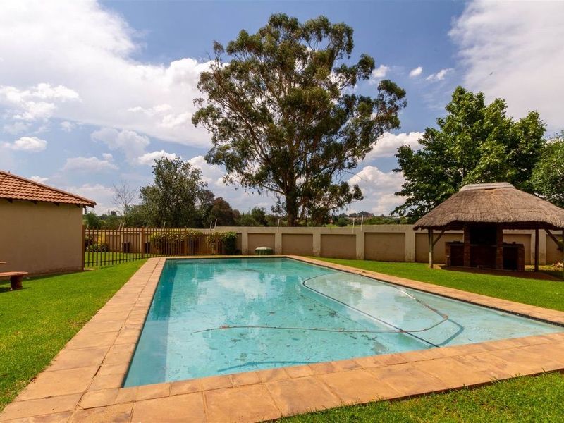 Outdoor pool area featuring a swimming pool with paved surround, a thatched lapa with a built-in braai, and a perimeter wall.