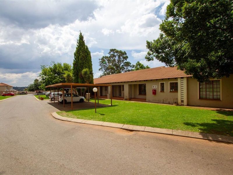 Exterior view of the apartment complex featuring a paved driveway, covered carport parking, and a well-maintained lawn area.