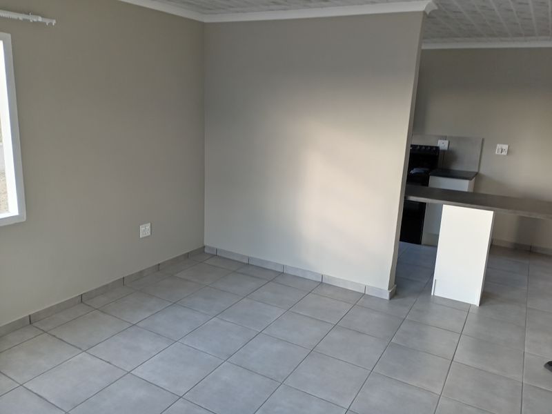 An open-plan living and kitchen area featuring neutral wall tones, tiled flooring, and a breakfast counter, providing a clean and functional living space.
