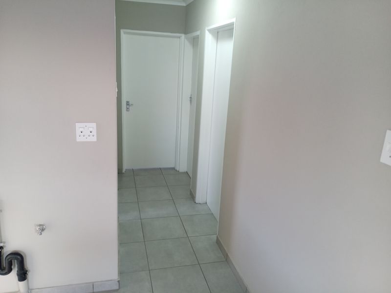 A clean, neutral-toned hallway featuring tiled flooring and multiple internal doors, providing access to various rooms within the home.