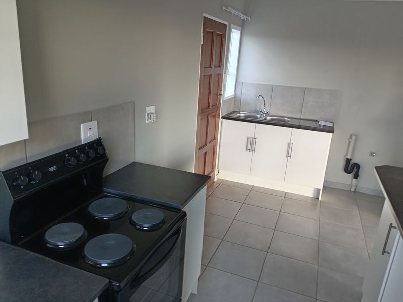 A functional kitchen featuring tiled flooring, built-in cabinetry, a stainless steel sink, and a freestanding electric stove.