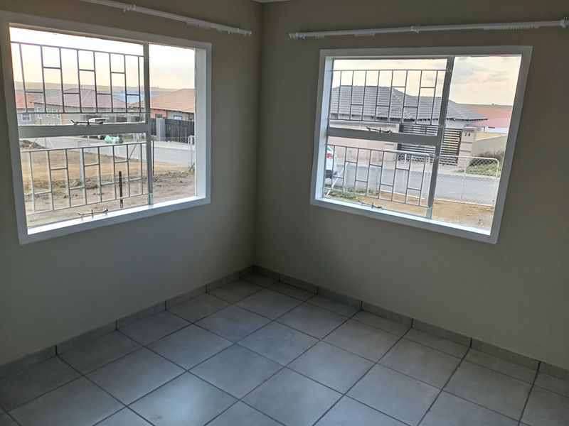 A bright, empty bedroom featuring neutral wall paint, tiled flooring, and large windows fitted with security bars.