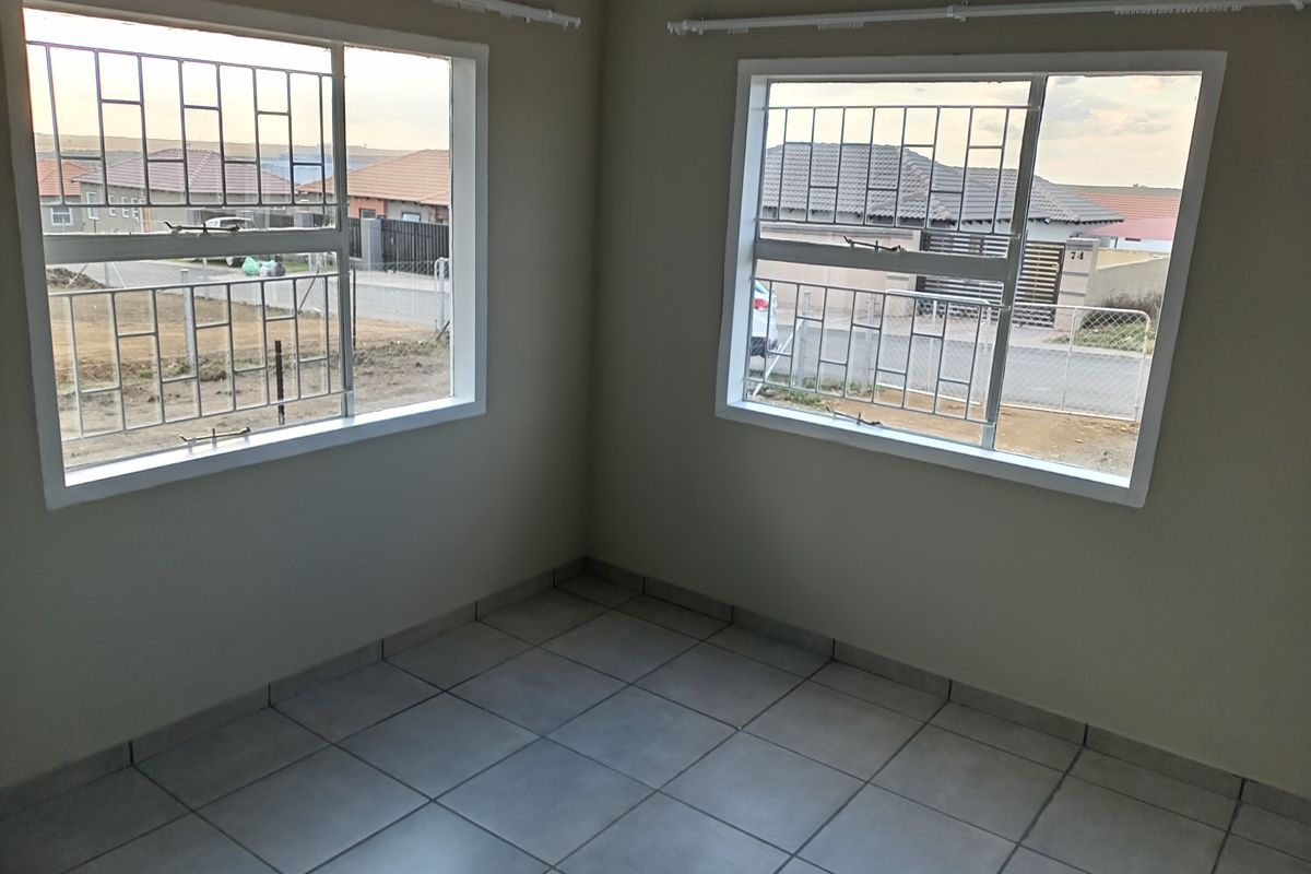 A bright, empty bedroom featuring neutral wall paint, tiled flooring, and large windows fitted with security bars.