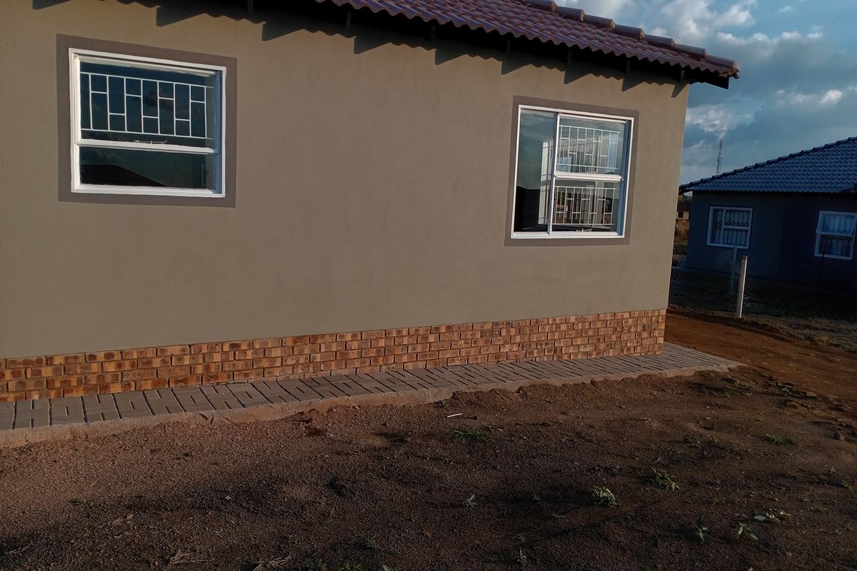 Side view of a modern house featuring a tiled roof, plastered walls with a brick base, and security-fitted windows.