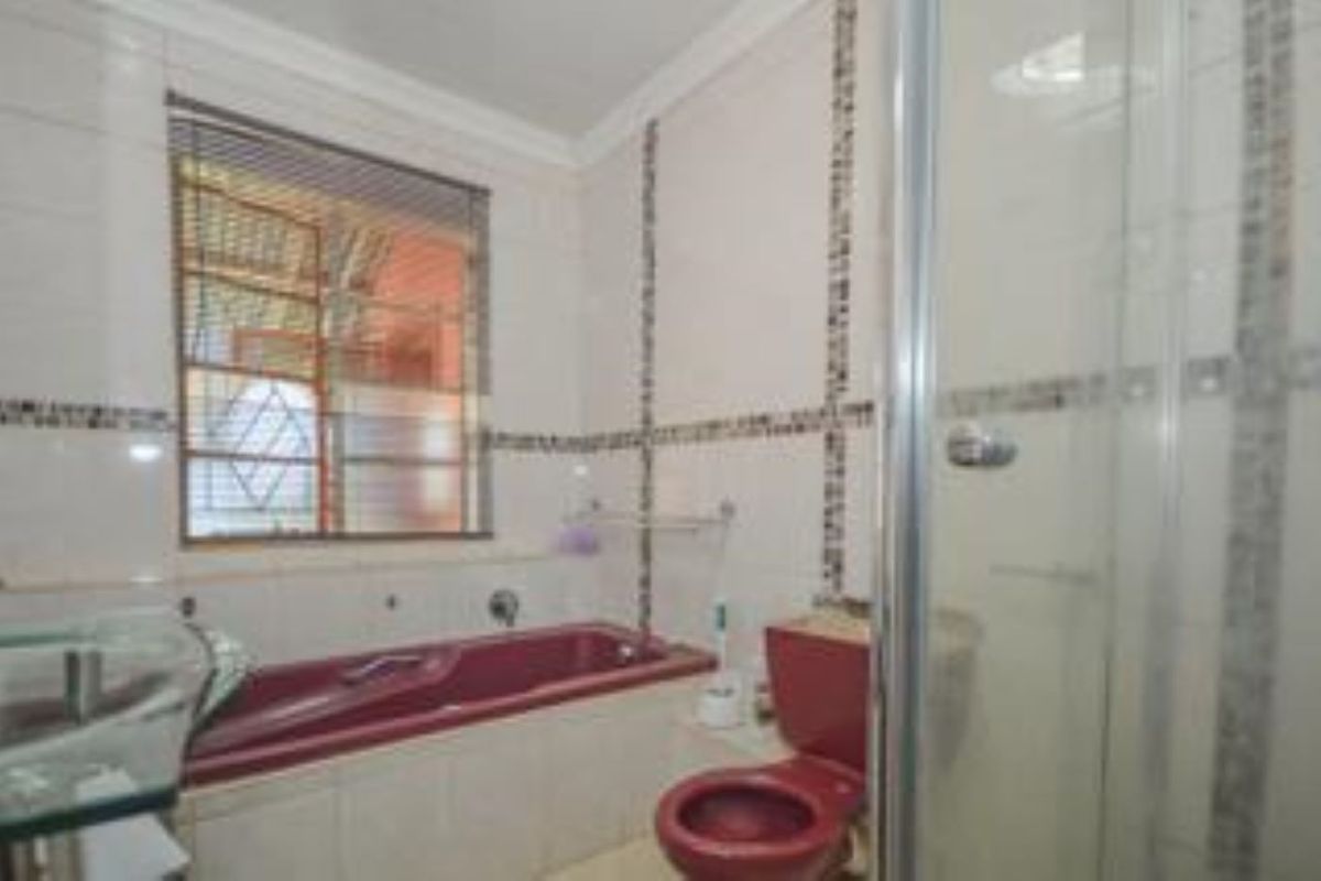 A dated bathroom featuring a maroon bathtub and matching toilet, glass shower enclosure, and tiled walls with decorative mosaic accents.