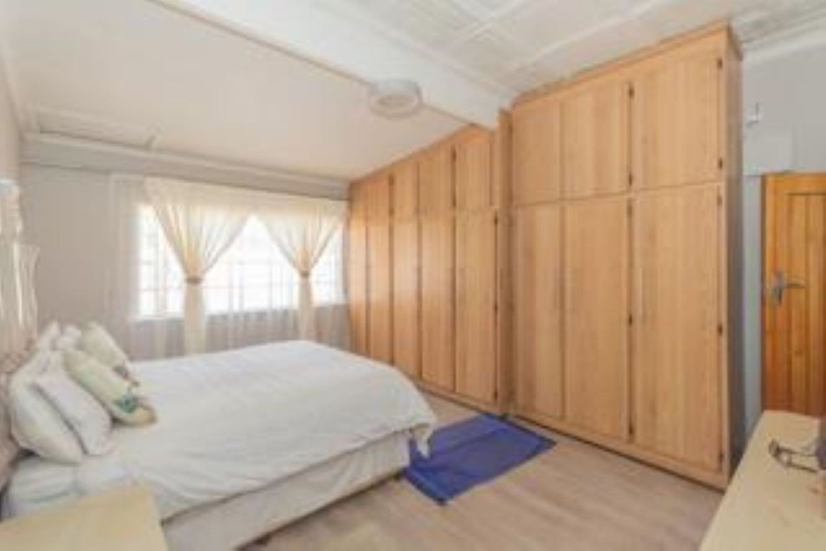A bedroom featuring extensive built-in wooden cabinetry, light-toned flooring, and a sloped ceiling with a central light fixture.