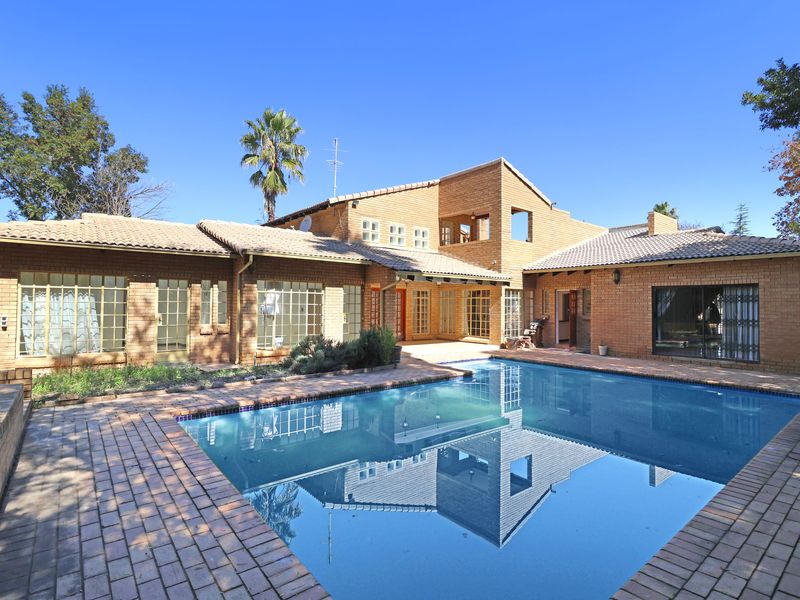 Spacious rear exterior view featuring a large swimming pool, brick facade, and multiple access points to the home's living areas.