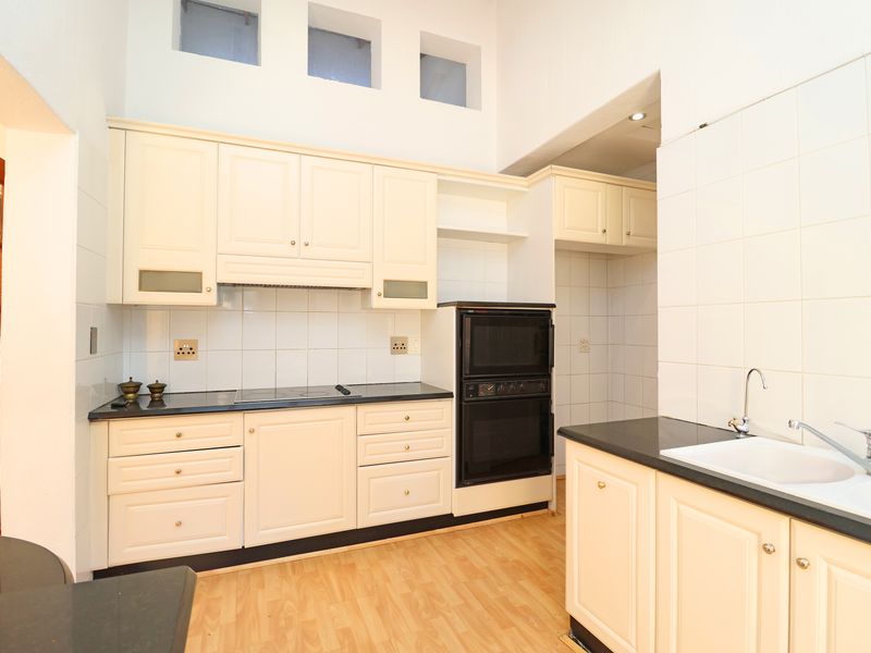 A functional kitchen featuring cream-colored cabinetry, dark countertops, a built-in double oven, electric hob, and a double sink with tiled splashbacks.