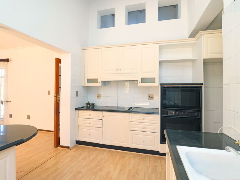 A functional kitchen featuring cream-colored cabinetry, dark countertops, a built-in oven, and a tiled backsplash, with an adjacent open-plan living area.