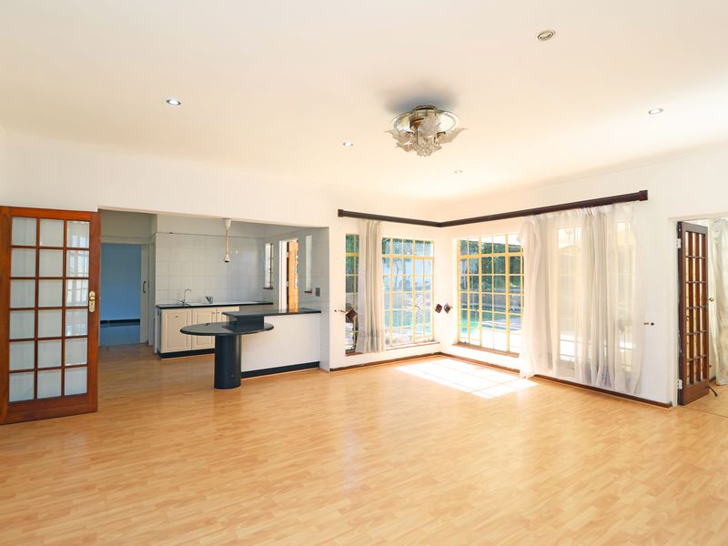 Spacious open-plan living area featuring laminate flooring, large windows with natural light, and a connected kitchen area with a breakfast bar.