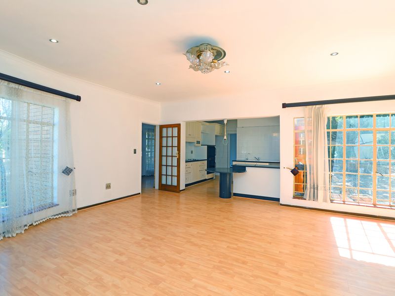 Spacious open-plan living area featuring laminate flooring, recessed lighting, and a connected kitchen with built-in cabinetry and a breakfast counter.