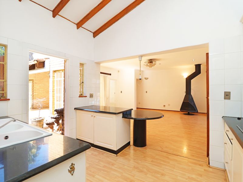 Open-plan kitchen and living area featuring a vaulted ceiling with exposed beams, a central island, and a freestanding fireplace in the adjacent living space.