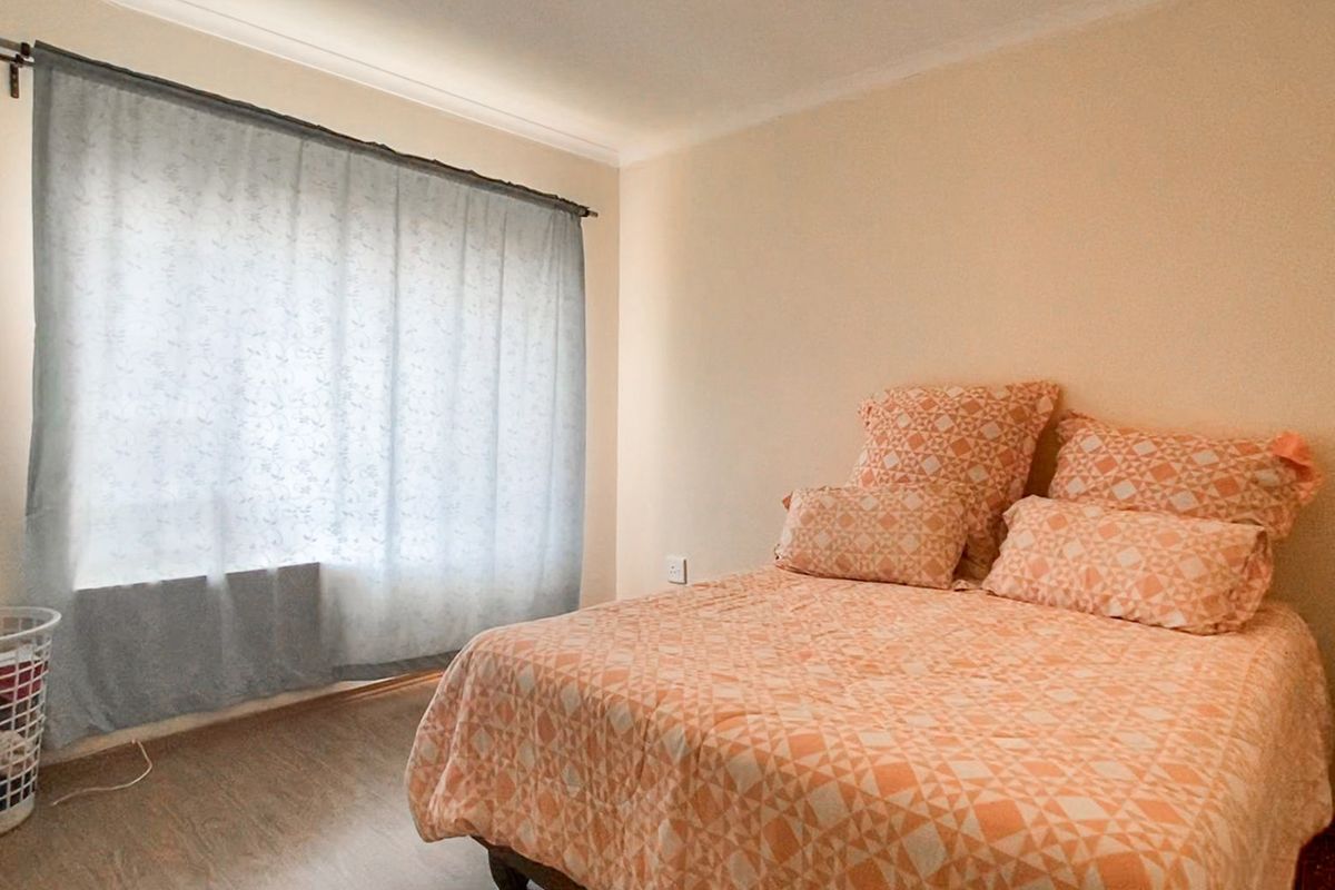 A simple bedroom featuring laminate flooring and a large window with a curtain rod, providing a neutral base for personalization.