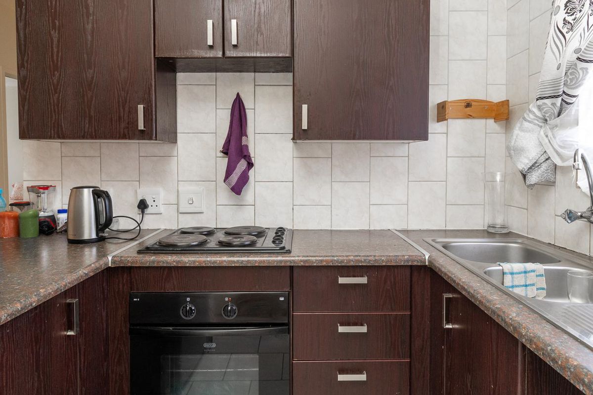 A functional kitchen featuring dark wood cabinetry, laminate countertops, a built-in electric oven, hob, and a stainless steel double sink with tiled backsplash.