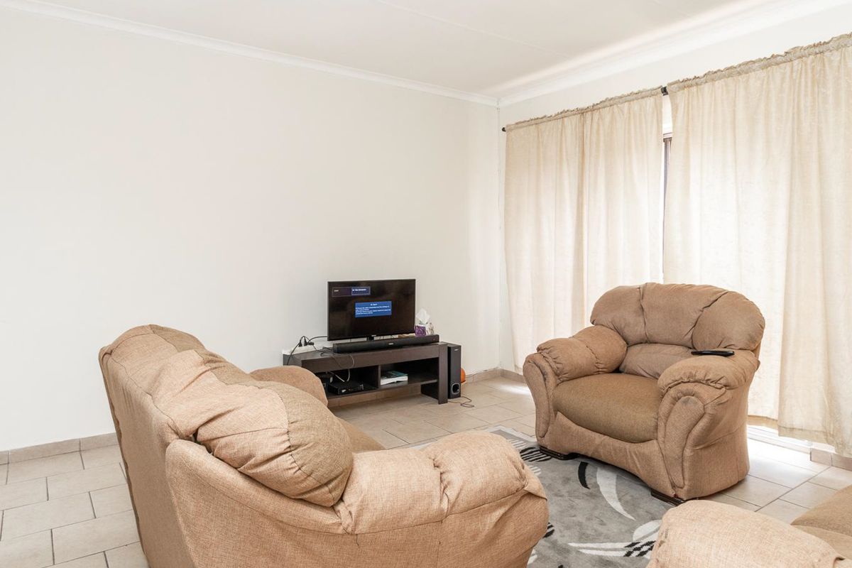 A functional living room featuring neutral tiled flooring and large windows with curtain tracks, providing a blank canvas for interior design updates.