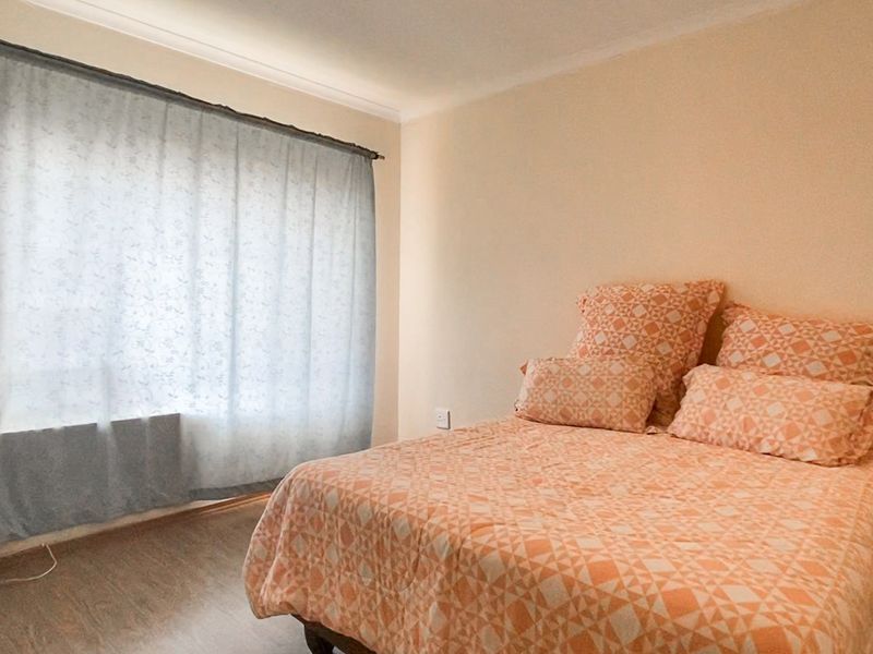 A simple bedroom featuring laminate flooring and a large window with a curtain rod, providing a neutral base for personalization.