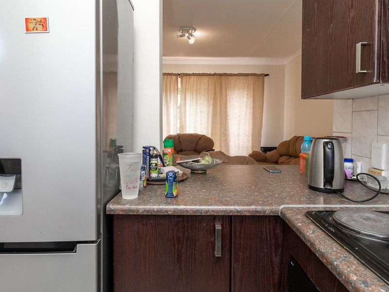 An open-plan kitchen area featuring dark wood cabinetry, laminate countertops, and an electric hob, looking through to the adjacent living space.