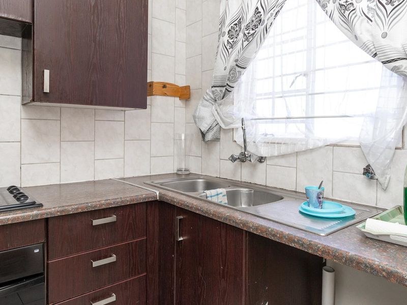 A functional kitchen featuring dark wood-look cabinetry, laminate countertops, a double stainless steel sink, and a built-in electric oven and hob.