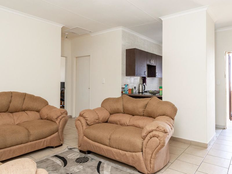 Open-plan living area featuring tiled flooring and a connected kitchen space with dark cabinetry and tiled backsplash.