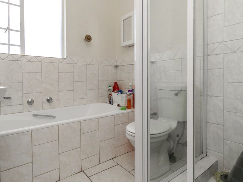 A functional bathroom featuring a bathtub, separate shower enclosure, and toilet with neutral wall and floor tiling.