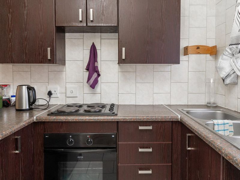 A functional kitchen featuring dark wood cabinetry, laminate countertops, a built-in electric oven, hob, and a stainless steel double sink with tiled backsplash.