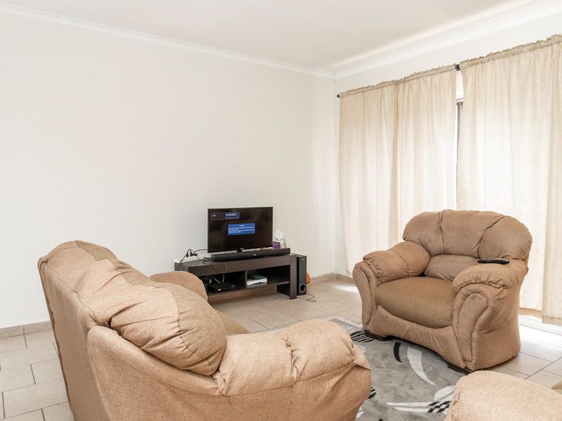 A functional living room featuring neutral tiled flooring and large windows with curtain tracks, providing a blank canvas for interior design updates.