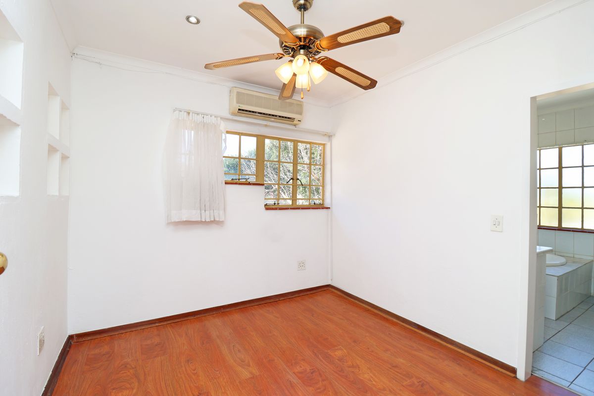 A bedroom featuring laminate flooring, a ceiling fan, and a wall-mounted air conditioning unit, with an adjoining bathroom visible through the doorway.