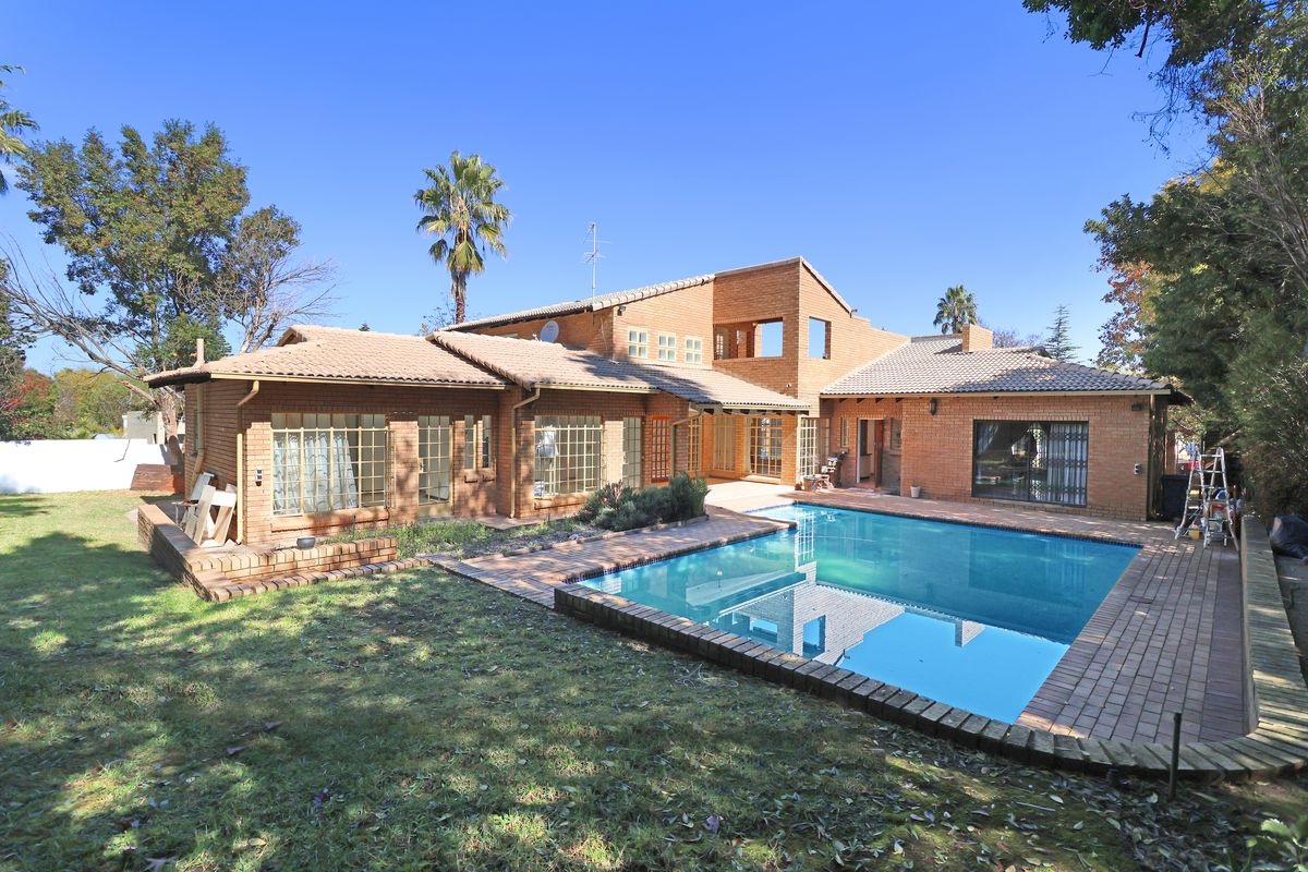 Rear view of a face-brick house featuring a swimming pool, paved patio area, and established garden.