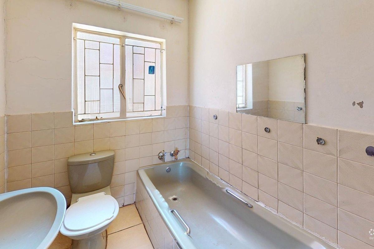 A dated bathroom featuring a bathtub, toilet, and wall-mounted mirror, requiring cosmetic updates and tile repairs to modernize the space.
