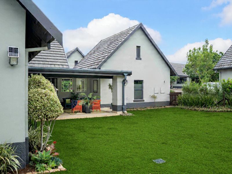A well-maintained rear exterior view featuring a covered patio area, manicured lawn, and established garden beds against a modern house structure.