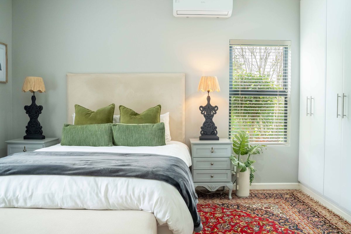 A well-maintained bedroom featuring built-in wardrobes, a wall-mounted air conditioning unit, and a window with fitted blinds.
