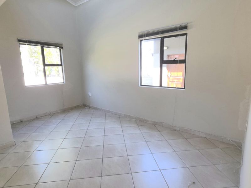 A vacant bedroom featuring neutral tiled flooring, aluminium window frames with fitted blinds, and high ceilings with coved cornicing.