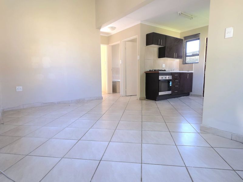 Open-plan living area featuring tiled flooring and a compact kitchen with built-in cabinetry, oven, and gas hob.