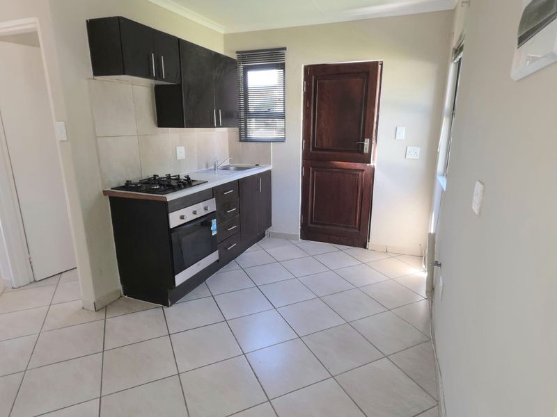 A compact kitchen featuring dark cabinetry, a gas hob, built-in oven, stainless steel sink, and tiled flooring with direct access to the exterior.