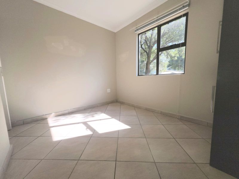 A bright, empty bedroom featuring neutral tiled flooring, clean walls, and a large window with natural light.