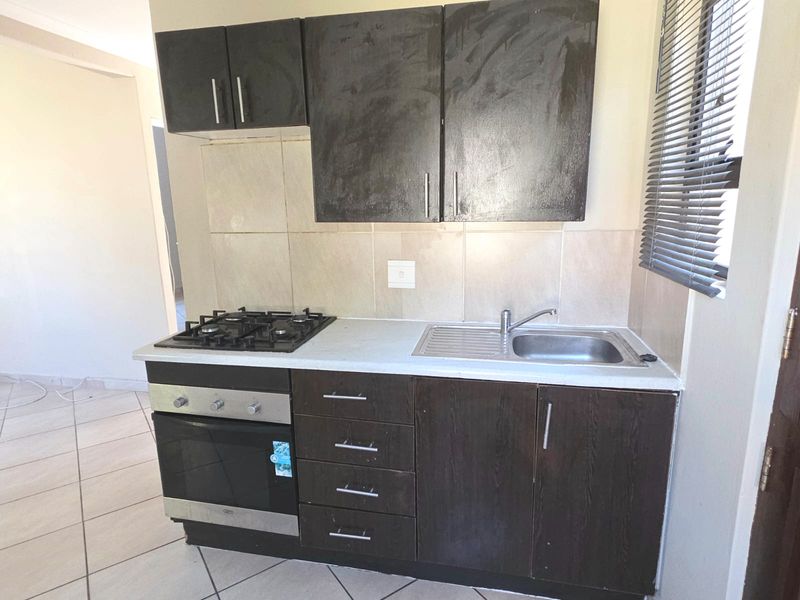Compact kitchen featuring dark built-in cabinetry, a gas hob, built-in oven, stainless steel sink, and tiled backsplash.