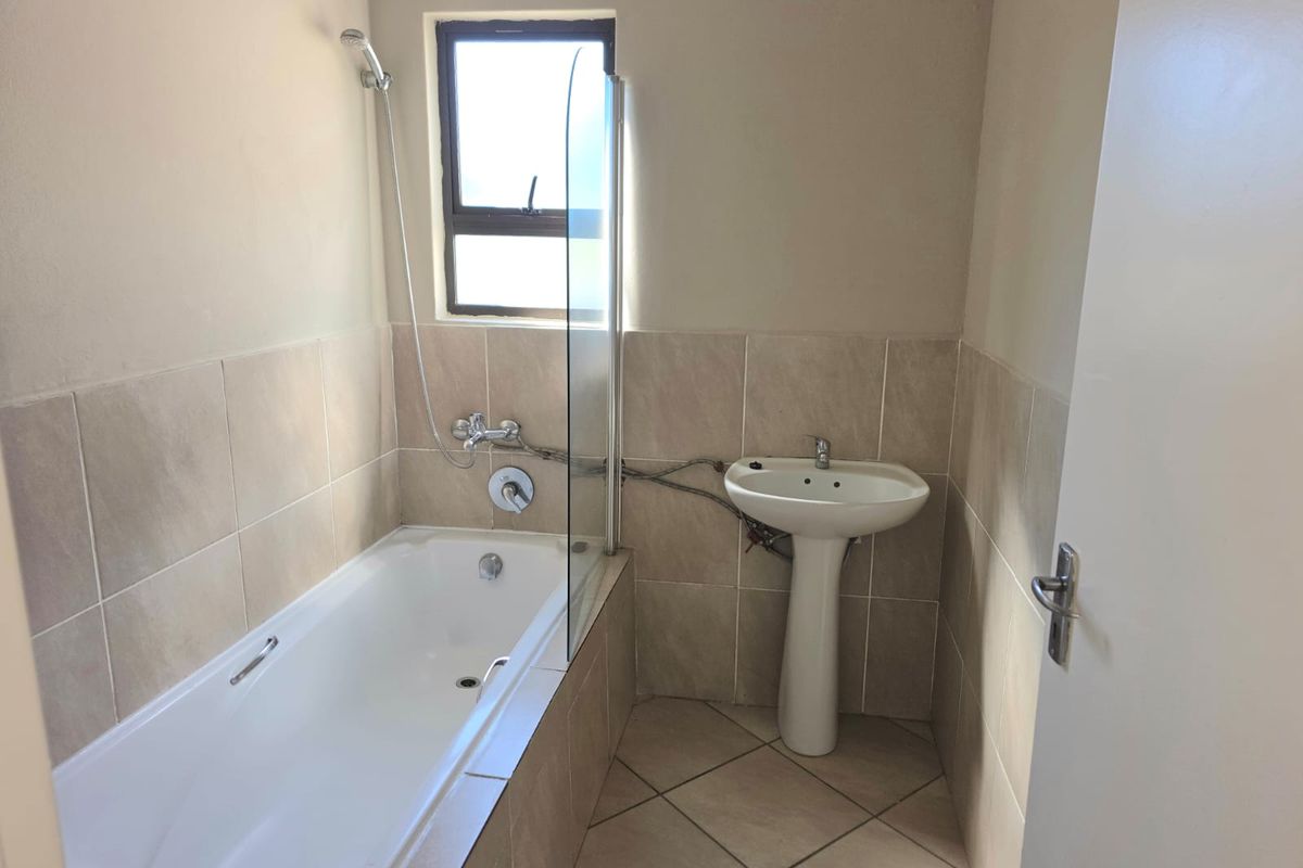 A functional bathroom featuring a built-in bathtub with a glass screen, a pedestal basin, and neutral tiled finishes.