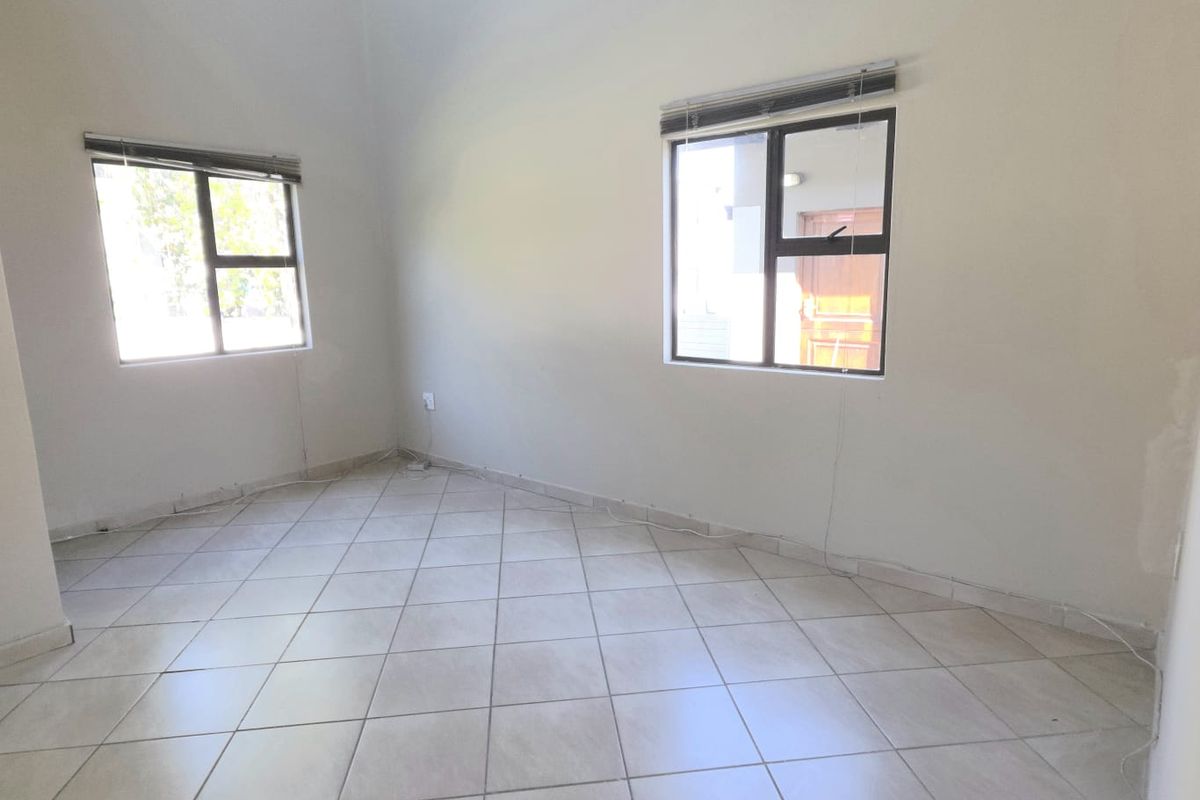 A vacant bedroom featuring neutral tiled flooring, aluminium window frames with fitted blinds, and high ceilings with coved cornicing.