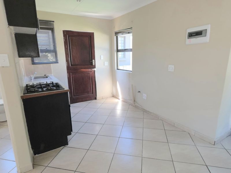 A functional kitchen area featuring tiled flooring, built-in cabinetry with a gas hob, and direct access to an exterior door.