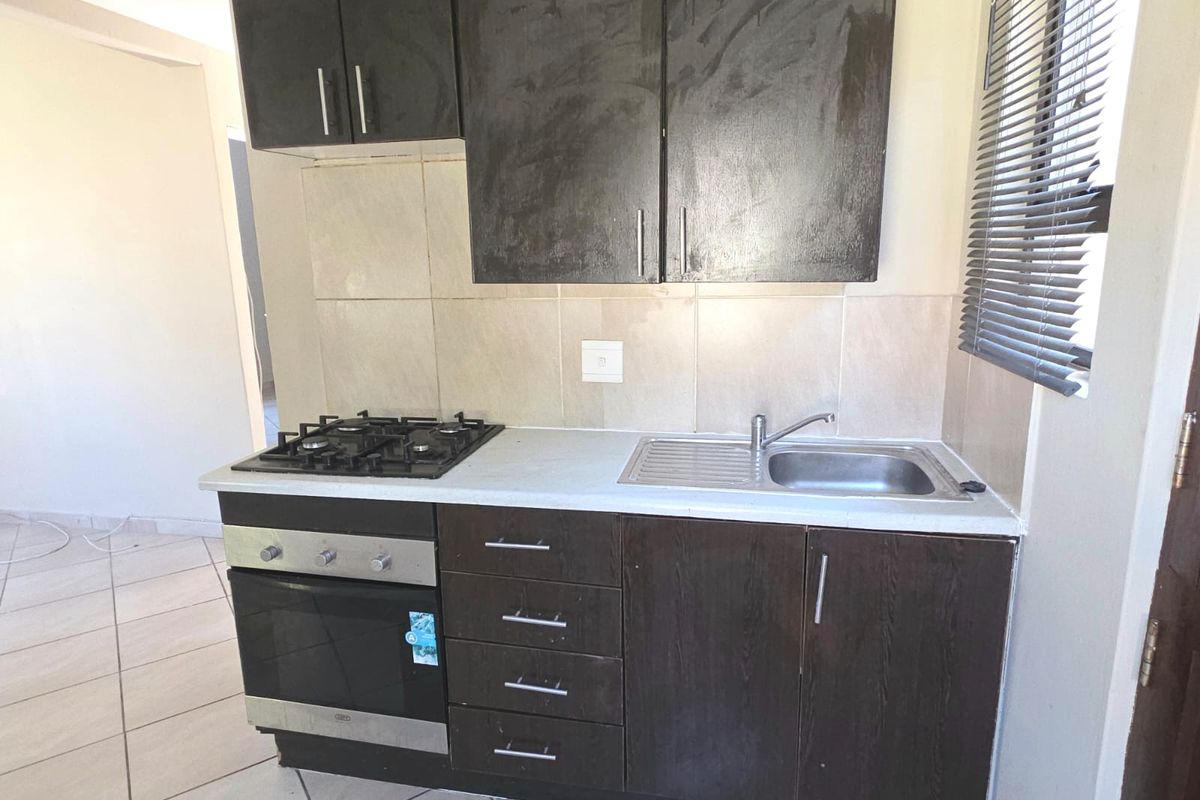 Compact kitchen featuring dark built-in cabinetry, a gas hob, built-in oven, stainless steel sink, and tiled backsplash.