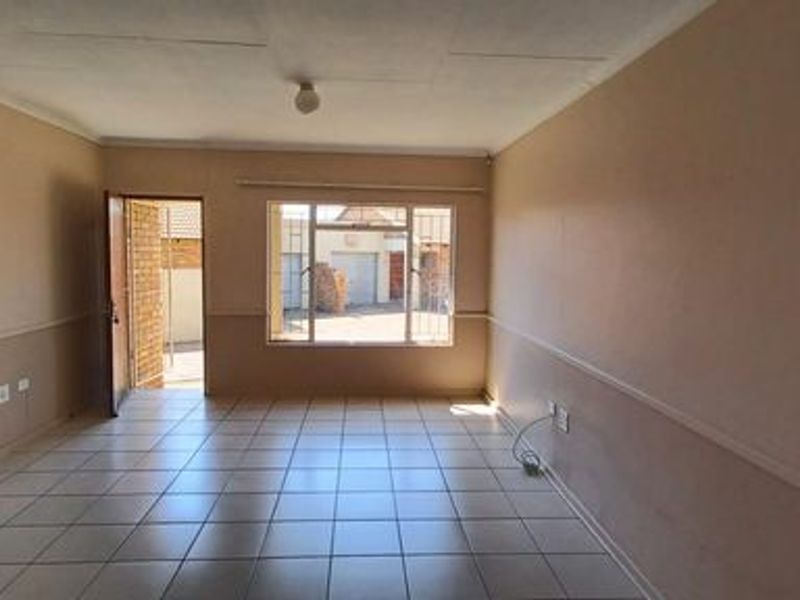 An empty, open-plan living area featuring tiled flooring, security bars on the windows, and neutral wall finishes, ready for personalization.