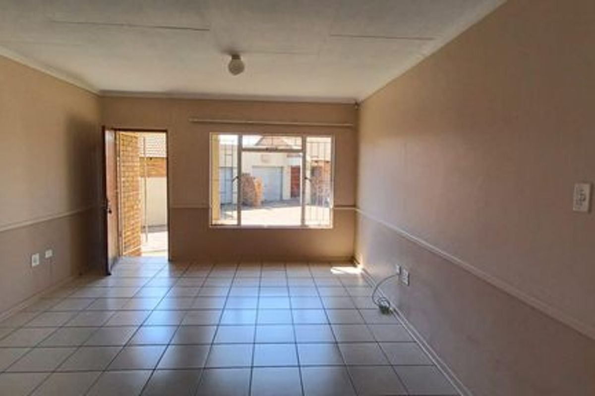 An empty, open-plan living area featuring tiled flooring, security bars on the windows, and neutral wall finishes, ready for personalization.