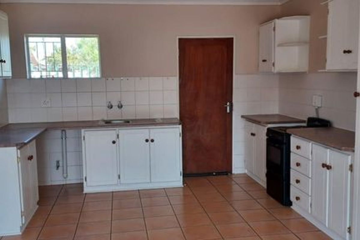 A functional kitchen featuring white cabinetry, tiled splashbacks, tiled flooring, and a freestanding stove, offering a blank canvas for potential modern updates.