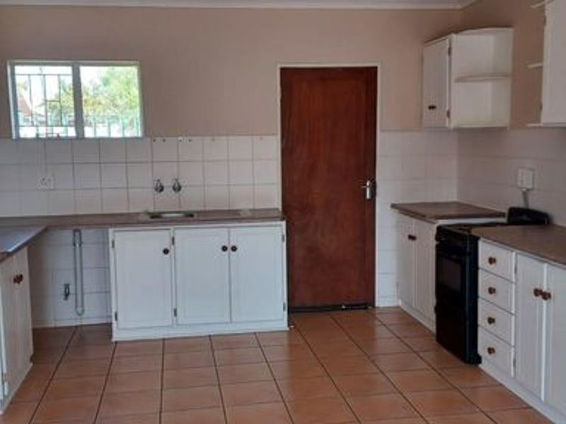 A functional kitchen featuring white cabinetry, tiled splashbacks, tiled flooring, and a freestanding stove, offering a blank canvas for potential modern updates.