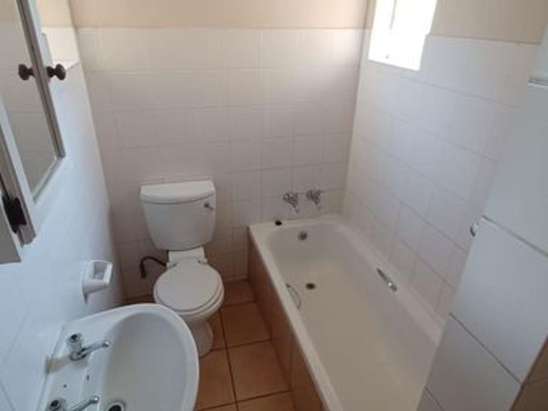 A functional bathroom featuring a bathtub, pedestal basin, and toilet with white wall tiling and neutral floor tiles.