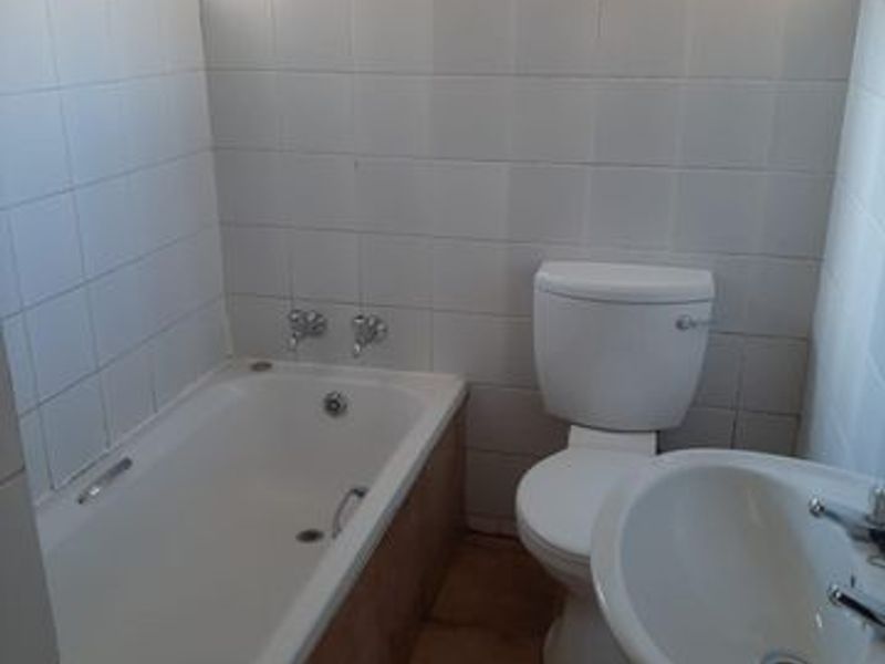A functional bathroom featuring a standard bathtub, pedestal sink, and toilet with white wall tiling and terracotta-style floor tiles.
